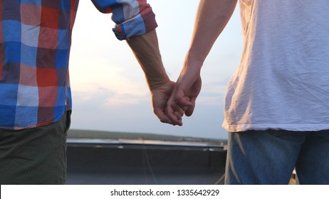 Rear View Of Male Couple Holding Hands Each Other And Jogging On Terrace Of Roof. Young Gay Boys Running To The Edge Of Rooftop And Raising Arms. Beautiful Cityscape At Background. Slow Motion.