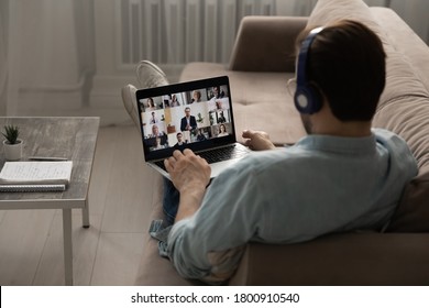 Rear view of male employee in headphones sit on couch at home office talk speak on video call on laptop with diverse colleagues, man have webcam digital virtual conference with coworkers on computer - Shutterstock ID 1800910540