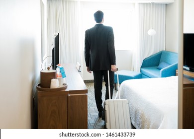 Rear view of male entrepreneur on business trip pulling suitcase while walking in room at hotel