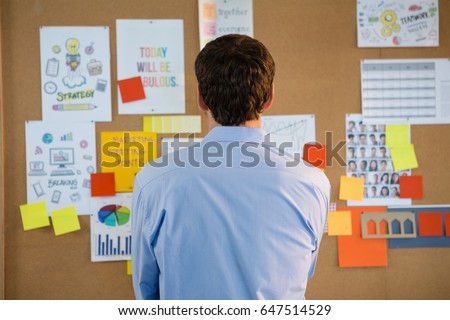 Rear view of male executive looking at the bulletin board in office