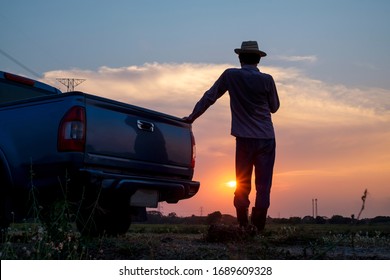 Rear view of male farmer standing looking at farmland at sunset, farm activity preparation, traveling by pickup truck