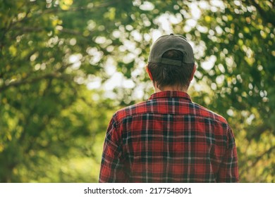 Rear view of male farmer wearing plaid shirt and trucker's hat standing in walnut orchard and looking at trees, selective focus - Shutterstock ID 2177548091