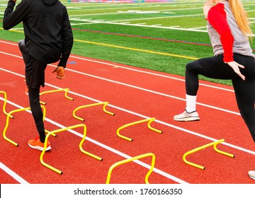 Rear view of male and a female athletes running over yellow mini hurdles set up in lanes on a red track at track and field practice. - Powered by Shutterstock