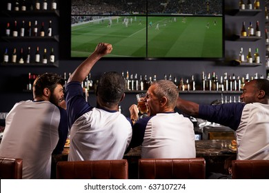 Rear View Of Male Friends Watching Game In Sports Bar