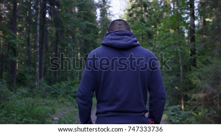 Rear view of male hiker standing in forest. Hooded young man standing in the forest and exploring, freedom and nature concept. Man back arms outstretched, autumn