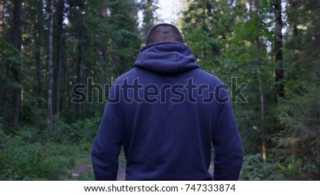 Rear view of male hiker standing in forest. Hooded young man standing in the forest and exploring, freedom and nature concept. Man back arms outstretched, autumn