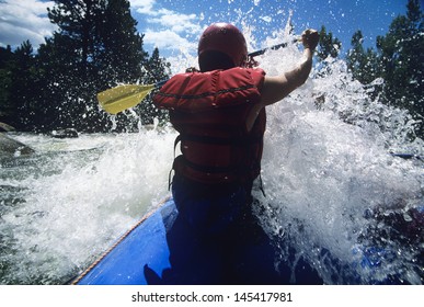 Rear View Of A Male Kayaker Paddling Through Rapids