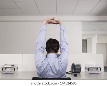 Rear View Of A Male Office Worker Stretching At Desk