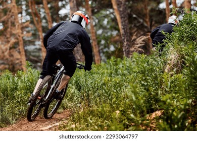 rear view male racer riding on forest trail downhill race, black sports clothes, biking high plants - Powered by Shutterstock