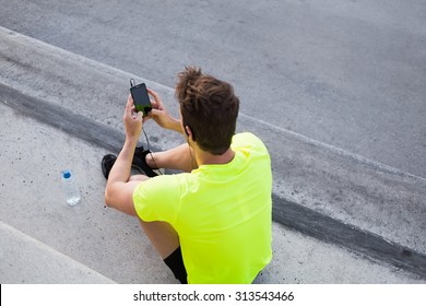 Rear view of male runner in bright t-shirt using mobile phone while taking break after active intense training outdoors, young sports man use smart phone with blank copy pace screen for text message - Powered by Shutterstock