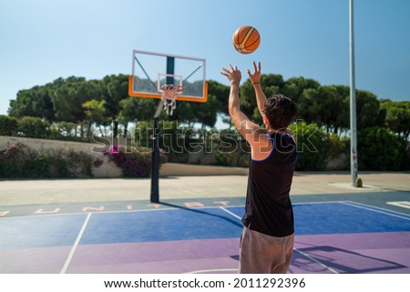 Rear view of male sportsman playing basketball throwing the ball at playground, view from behind. Precision shot