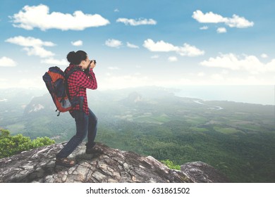 Rear view of male traveler standing on the mountain while taking photo and carrying backpack