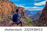 Rear view of man with backpack sitting on rock along Bright Angel trail with aerial overlook of South Rim of Grand Canyon National Park, Arizona, USA, America. Amazing vista after sunrise in summer