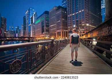 Rear view of man with backpack while walking on bridge and looking around. Illuminated city with skyscrapers at twilight. Chicago, United States. - Powered by Shutterstock