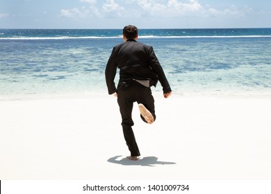 Rear View Of A Man In Black Suit Running Barefoot Toward The Sea At Beach