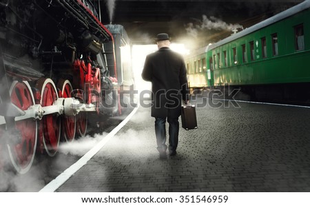 Rear view of man in bowler hat with suitcase walking on the platform next to steaming locomotive