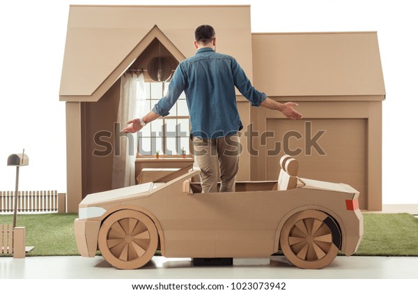rear view of man in cardboard car in front of\
cardboard house isolated on\
white