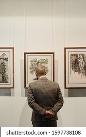 Rear View Of Man In Formal Wear Standing And Looking At Paintings On The Wall At Art Gallery