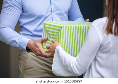 Rear View Of A Man Giving Gift Box To His Smiling Neighbor Standing At Doorway