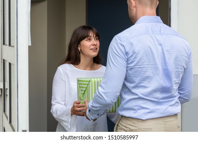 Rear View Of A Man Giving Gift Box To His Smiling Neighbor Standing At Doorway