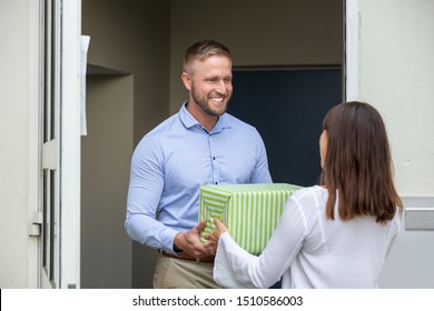 Rear View Of A Man Giving Gift Box To His Smiling Neighbor Standing At Doorway