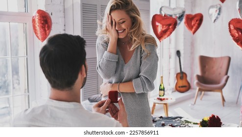 Rear view of man holding engagement ring while making proposal to his happy girlfriend - Powered by Shutterstock