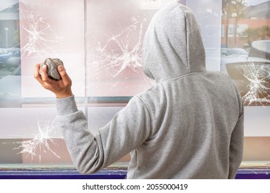 Rear View Of A Man Holding A Stone To Throw It Against A Glass And Break A Window.