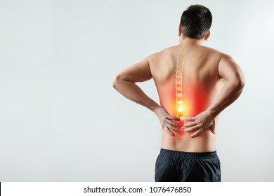 Rear view, the man holds his hands behind his back, pain in the back, pain in the spine, highlighted in red. Light background. The concept of medicine, massage, physiotherapy, health. - Shutterstock ID 1076476850