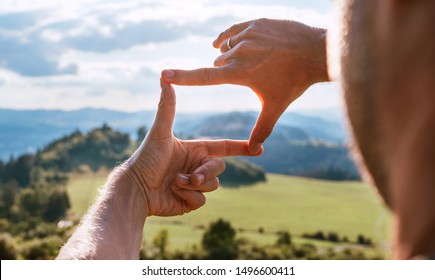 Rear view of Man looking at mountain landscape framing with fingers, searching for best image composition as he hiking over the mountain range. Landscape photographer or moviemaker occupation concept. - Powered by Shutterstock