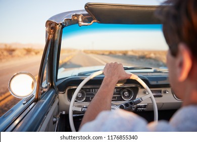 Rear View Of Man On Road Trip Driving Classic Convertible Car Towards Sunset