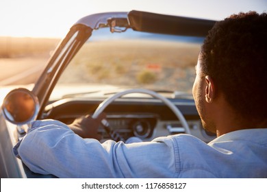 Rear View Of Man On Road Trip Driving Classic Convertible Car Towards Sunset