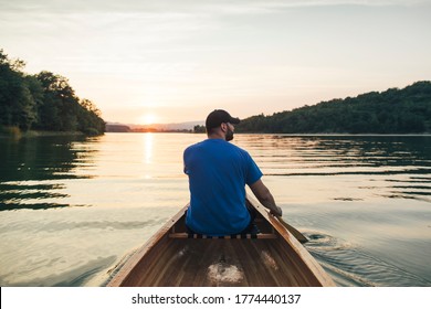 Rear View Of Man Paddling Canoe In The Forest Lake