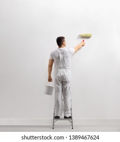 Rear View Of A Man Painting A Wall On A Ladder Isolated On White Background