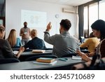 Rear view of man raising arm to ask a question during a presentation in lecture hall. 