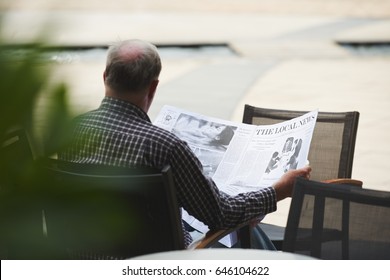 Rear View Of Man Reading News In Local Newspaper