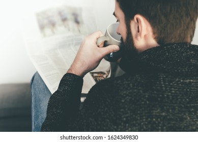 Rear View Of Man Reading Newspaper While Relaxing On Couch.