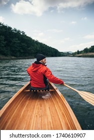 Rear view of man in red jacket paddling canoe on cloudy day