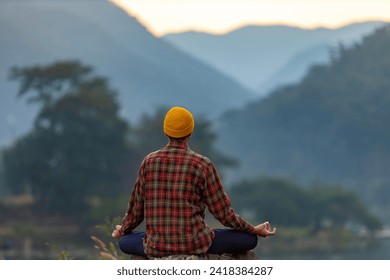 Rear view of man is relaxingly practicing meditation yoga in forest in summer to attain happiness from inner peace wisdom with morning light for healthy mind and soul concept