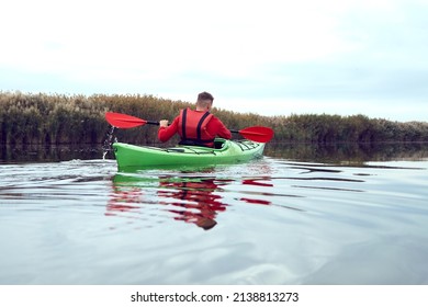 Rear view of man rowing in a green kayak in the river near bulrush at calm autumn day