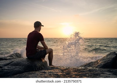 Rear view of man sitting on rock and watching beautiful sunset over ocean.
 - Powered by Shutterstock