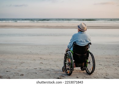 Rear view of man sitting on wheelchair and enjoying view at sea. - Powered by Shutterstock