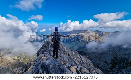 Rear view of man with speeding arms on cloud covered mountain summit of Mytikas Mount Olympus, Mt Olympus National Park, Macedonia, Greece, Europe. View of rocky ridges and Mediterranean Aegean Sea