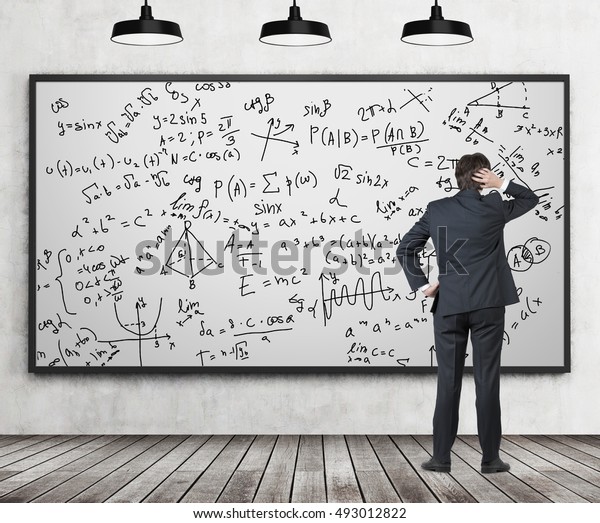 Rear view of man in suit staring at whiteboard with formulas in confusion. Classroom with concrete wall and wooden floor. Concept of exact sciences and studying. 