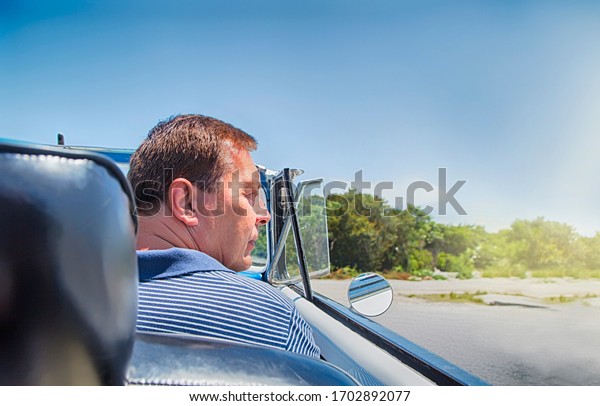 Rear\
view of man in vintage classic american car in\
Cuba.