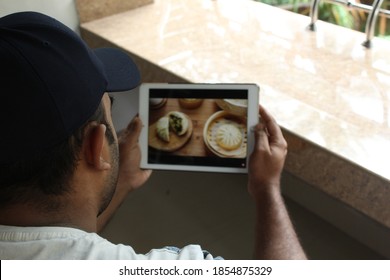 Rear View Of Man Wearing Cap, Sitting And Watching Cooking Video In Tablet