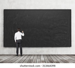 Rear view of the man who is going to write something on the black chalkboard. Wooden floor and concrete wall. A concept of the beginning of new academic year. A class room. - Powered by Shutterstock