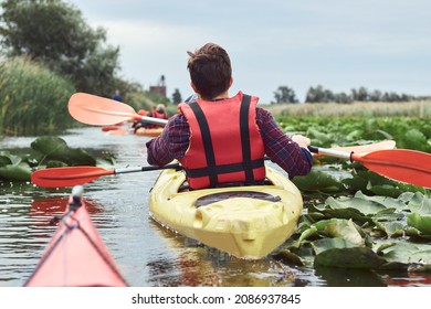 Rear view of man and a woman paddle yellow kayak on a lake with green leaves of water lilies at summer