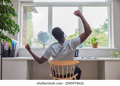 Rear View Of Man Working From Home On Computer  In Home Office Stretching At Desk