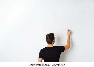 Rear View Of Man Writing On White Wall With Copy Space