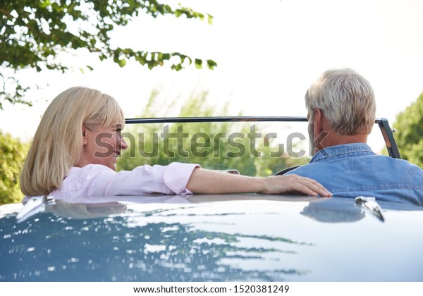 Rear View Of Mature Couple\
Enjoying Road Trip In Classic Open Top Sports Car Together         \
